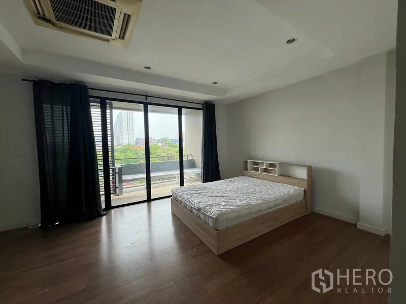 Townhouse for rent or sale in Khlong Toei, Bangkok - Spacious master bedroom opening to a balcony with city view and wood floors.