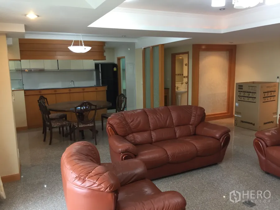Condominium for rent in Watthana, Bangkok - Spacious open-plan living and dining area with leather sofas, round table, and a built-in kitchen counter under recessed lighting.