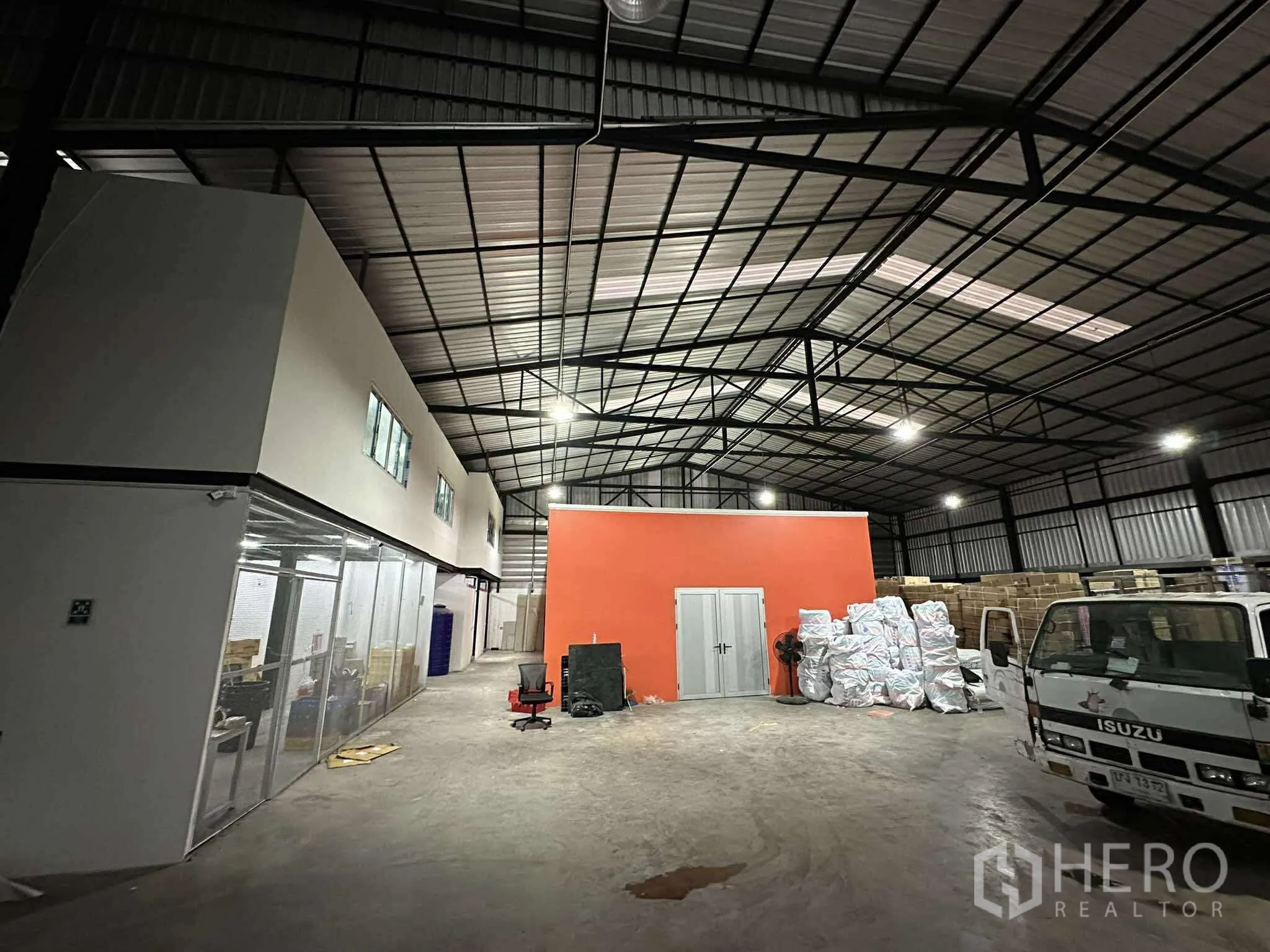 Warehouse for rent - Spacious high-ceiling warehouse with steel truss roof, central loading zone and an orange partition room.