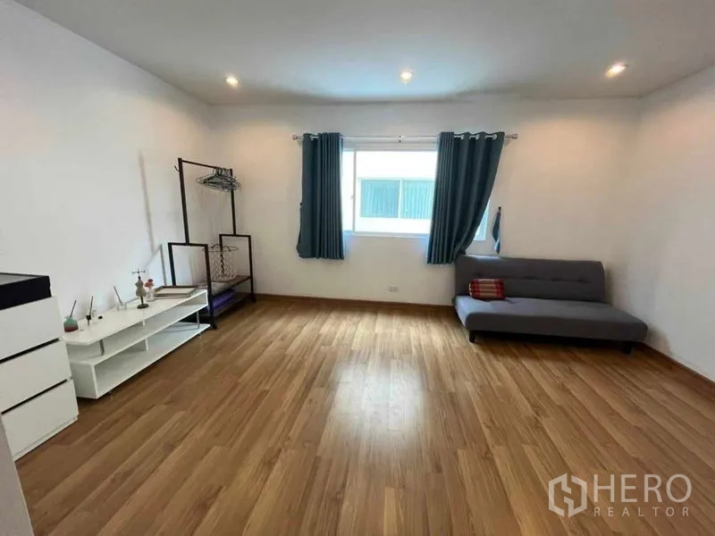 Townhouse for rent in Suan Luang, Bangkok - Spacious multipurpose room with sofa, window and wood laminate floor.