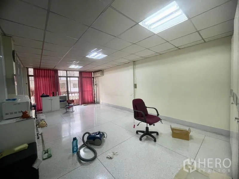 Townhouse for rent in Sathon, Bangkok - Open multi-purpose room with tiled floor, red curtains and fluorescent ceiling lights.