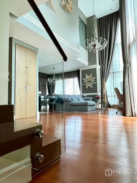 Condominium for rent in Khlong Toei, Bangkok - Wood staircase leading to an airy living room with high ceilings and large windows.