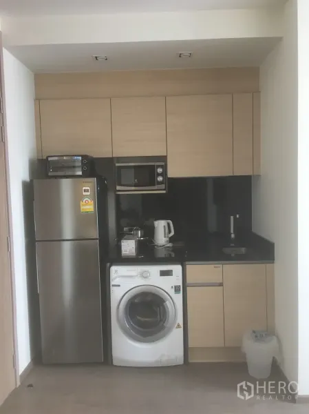Condominium for rent or sale in Khlong Toei, Bangkok - Compact kitchen with fridge, microwave, washing machine and black stone countertop.