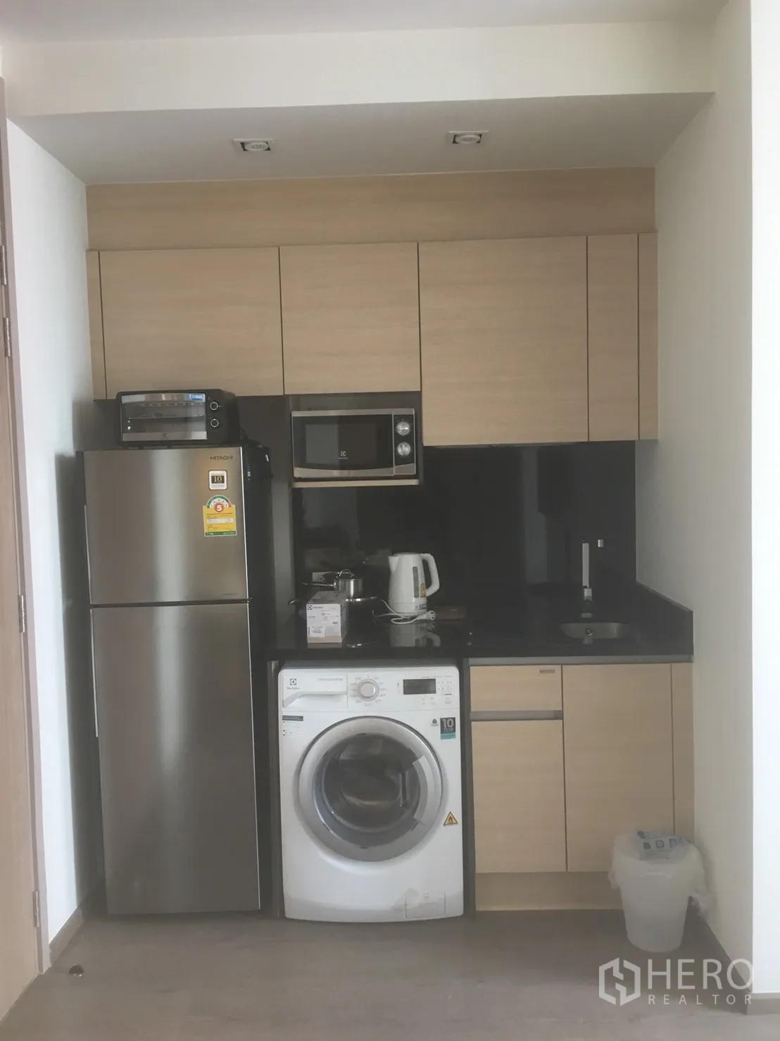 Condominium for rent or sale in Khlong Toei, Bangkok - Compact kitchen with fridge, microwave, washing machine and black stone countertop.