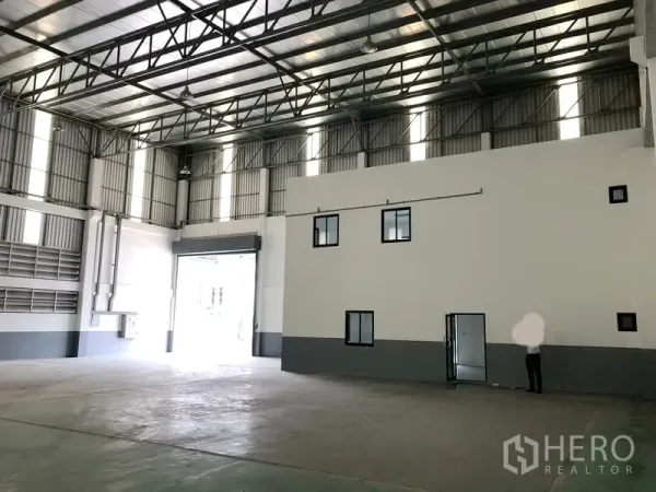 Factory for rent or sale in Samut Prakan - Warehouse hall showing a two-storey internal office block and a large roller shutter door.