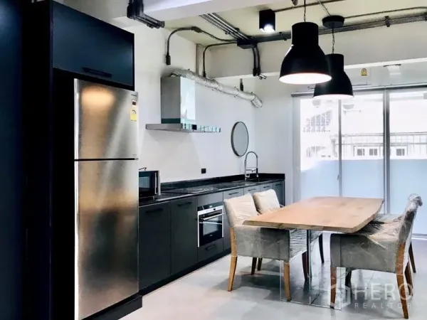 Townhouse for rent or sale in Khlong Toei, Bangkok - Industrial-style kitchen with black cabinetry, stainless fridge, oven and pendant lights.