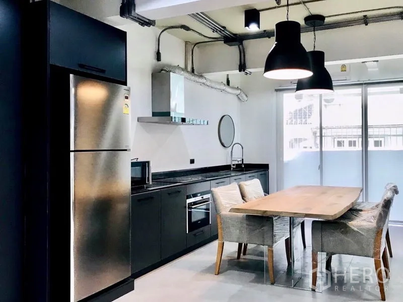 Townhouse for rent or sale in Khlong Toei, Bangkok - Industrial-style kitchen with black cabinetry, stainless fridge, oven and pendant lights.
