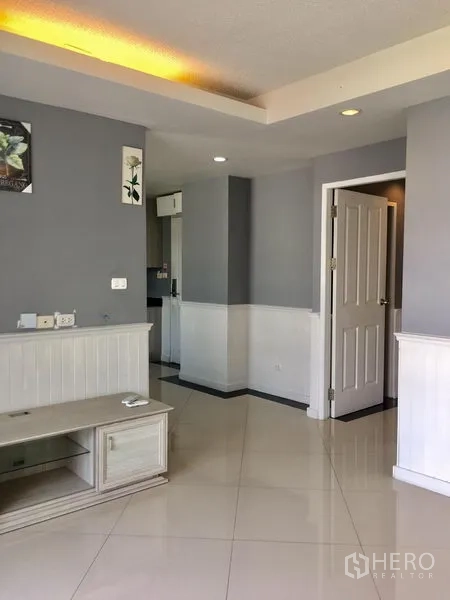 Condominium for rent in Khlong Toei, Bangkok - Entry to living area showing TV stand, doorway and glossy tiled floors.