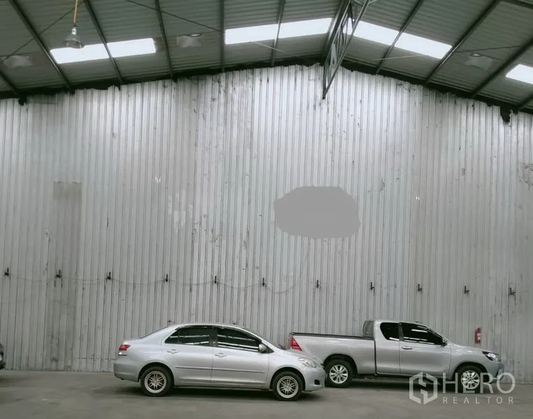 Warehouse for rent in Khlong Luang, Pathum Thani - High-ceiling warehouse interior with corrugated metal wall, skylights and parked cars on a smooth concrete floor.