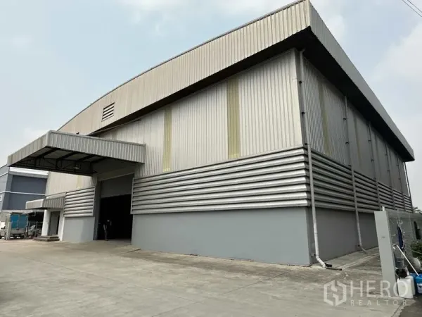 Warehouse for rent in Bang Phli, Samut Prakan - Corner view of metal-clad warehouse showing covered loading bay and truck access.