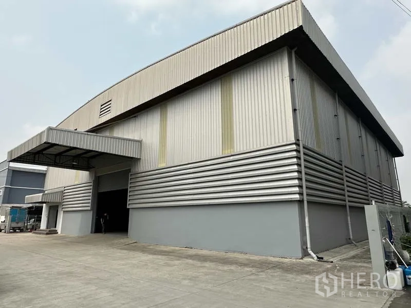 Warehouse for rent in Bang Phli, Samut Prakan - Corner view of metal-clad warehouse showing covered loading bay and truck access.