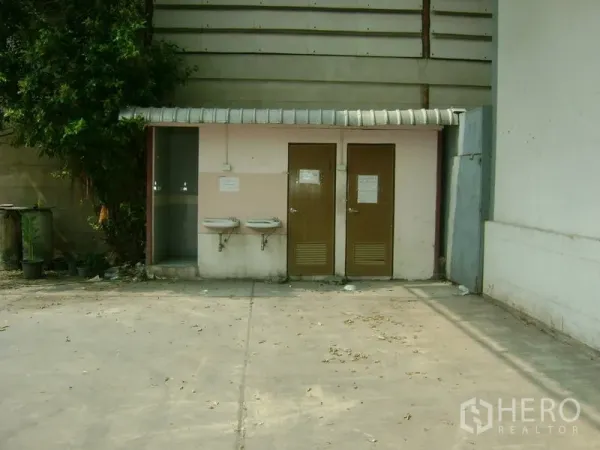 Warehouse for rent in Mueang Samut Sakhon, Samut Sakhon - Outdoor staff restroom block with two doors and wall-mounted sinks beside the warehouse yard.