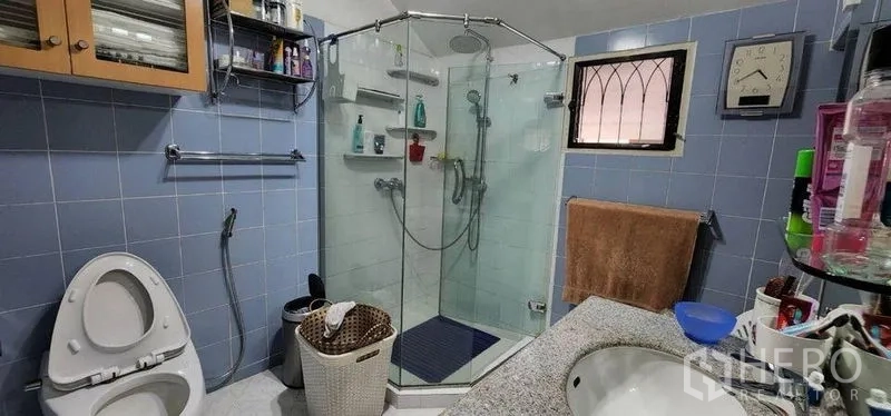 Detached House for rent in Bang Kapi, Bangkok - Blue-tiled bathroom with corner glass shower, toilet and vanity.