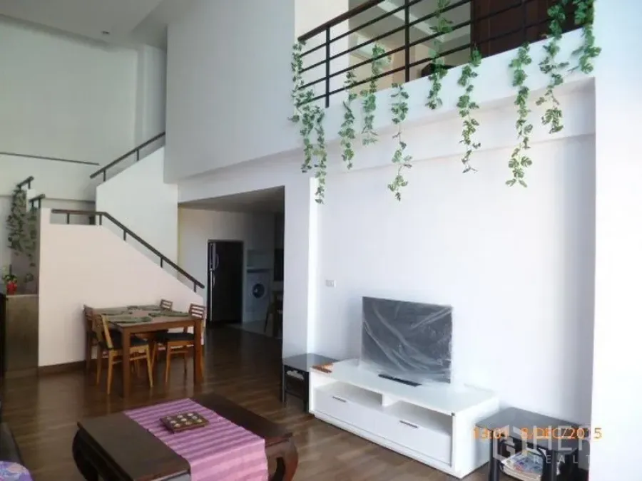 Condominium for rent in Pathum Wan, Bangkok - Bright double-height living and dining area with TV console, staircase to mezzanine and hanging greenery.