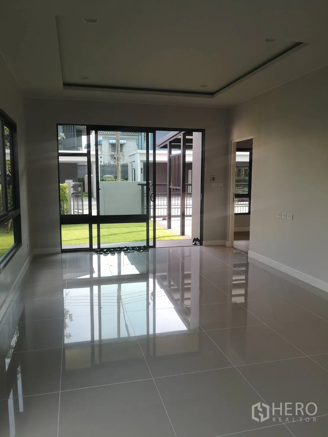 Detached House for sale in Lam Luk Ka, Pathum Thani - Ground-floor living room with glossy tile flooring and sliding doors opening to the lawn.