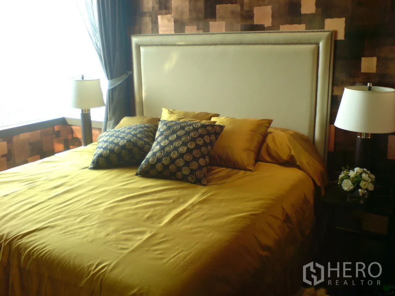 Condominium for rent in Khlong Toei, Bangkok - Primary bedroom with upholstered headboard, gold bedding and bedside lamps.
