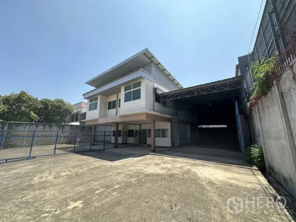 Warehouse for rent in Bueng Kum, Bangkok - Driveway view of warehouse showing ample parking and covered loading entrance on the right.