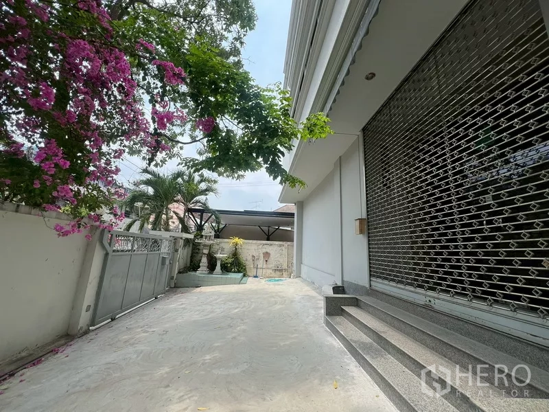 Warehouse for rent in Phra Khanong, Bangkok - Shaded driveway beside the building with grille shutter, gate and small garden planters