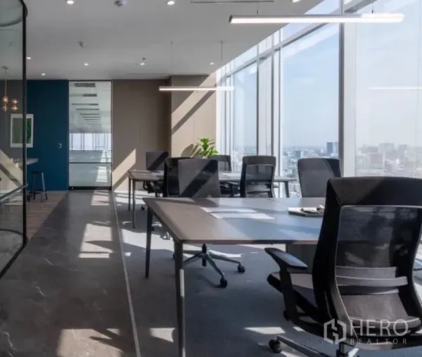Office Space for rent - Open-plan workstations beside a glass partition and large windows, illuminated by modern linear lights.