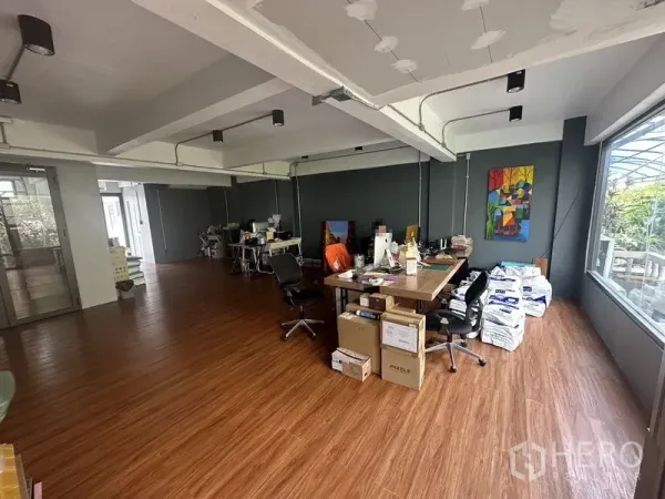 Home Office for rent in Sathon, Bangkok - Open-plan workspace with wood floors, exposed beams and a large window providing natural light.