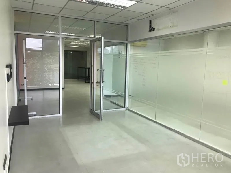 Office Space for rent in Khlong Toei, Bangkok - Hallway with glass partitions leading to a meeting room with a hinged glass door and frosted panels.