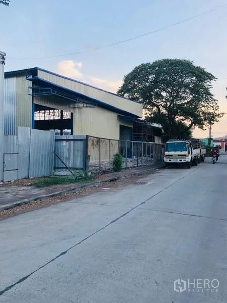 Warehouse for rent in Bang Kapi, Bangkok - Side view of warehouse along a quiet road with truck parking and a mature tree.