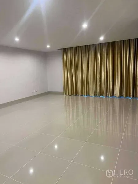 Home Office for rent in Bang Khen, Bangkok - Spacious empty room with glossy tile floors, recessed lighting, and gold curtains suited for workspace.