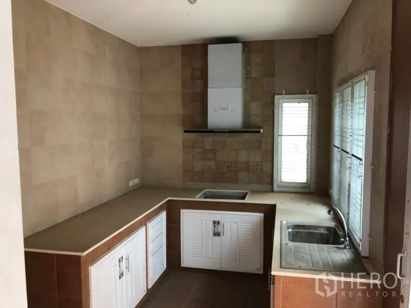 Detached House for sale in Bang Khen, Bangkok - Built-in Thai kitchen with L-shaped counters, sink, stove space and cooker hood beside shuttered windows.