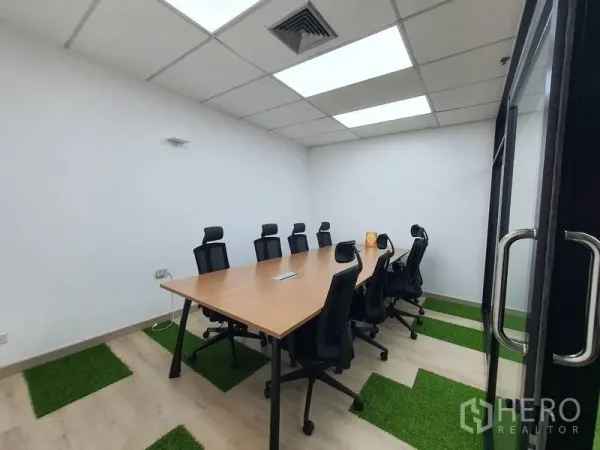 Office Space for rent - Glass-door meeting room for eight with ceiling lights, rectangular table and green turf floor accents.