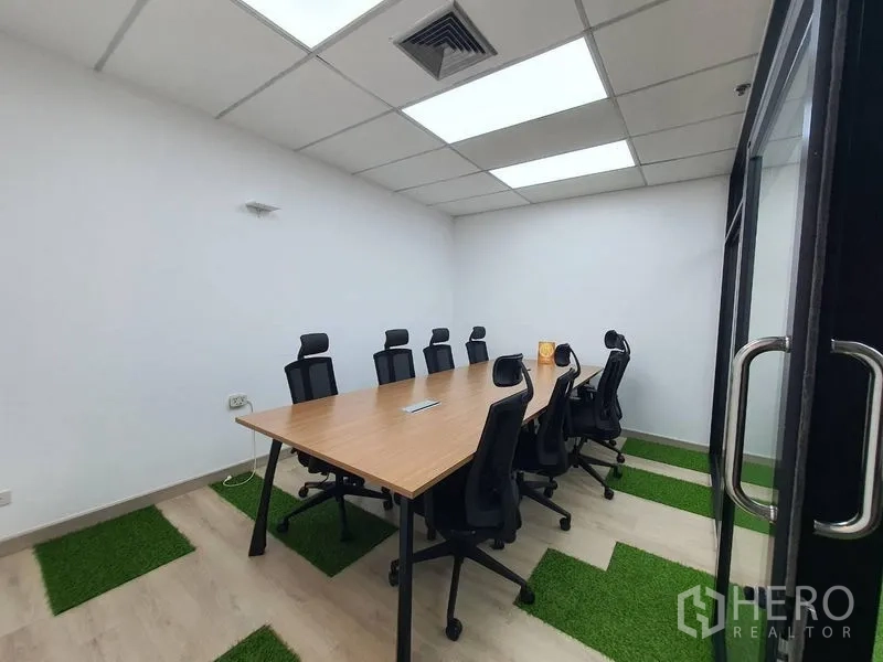 Office Space for rent - Glass-door meeting room for eight with ceiling lights, rectangular table and green turf floor accents.