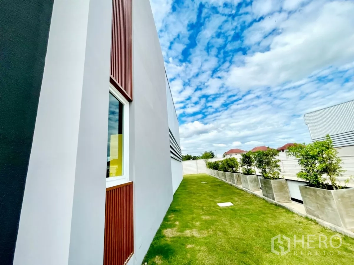 Warehouse for sale in Lam Luk Ka, Pathum Thani - Side elevation of office and warehouse with grass yard, planters and privacy wall.