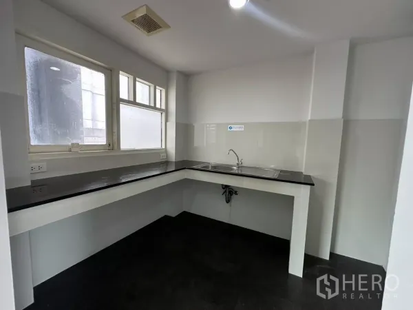 Office Space for rent in Watthana, Bangkok - Pantry with L-shaped black countertop, stainless sink and daylight from corner windows.