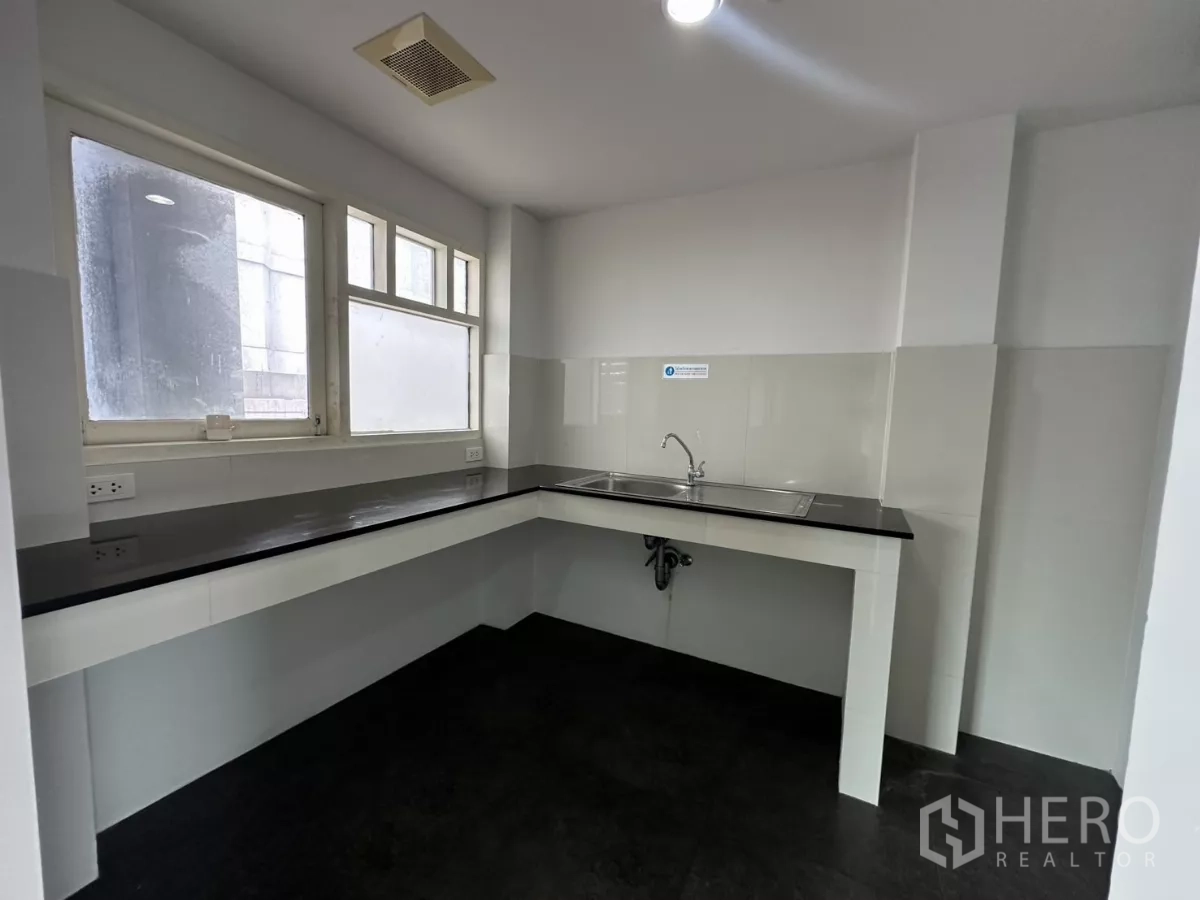 Office Space for rent in Watthana, Bangkok - Pantry with L-shaped black countertop, stainless sink and daylight from corner windows.