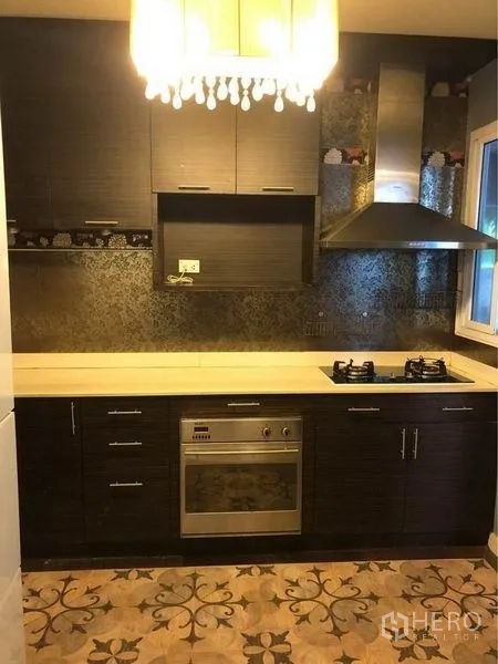 Detached House for rent or sale in Prawet, Bangkok - Fitted kitchen with dark cabinetry, gas hob, oven, range hood, and patterned floor.