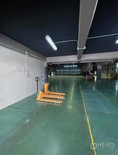 Warehouse for rent in Si Racha, Chon Buri - Ground-level storage zone with pallet jacks and strip lighting inside the warehouse.