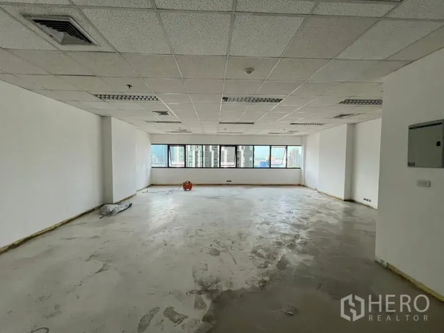 Office Space for rent in Watthana, Bangkok - Spacious shell office with concrete subfloor, white walls, and multiple windows overlooking Bangkok skyline.
