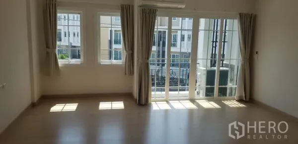 Townhouse for rent in Bang Na, Bangkok - Spacious bedroom with large windows, balcony doors, curtains, and an air conditioner.
