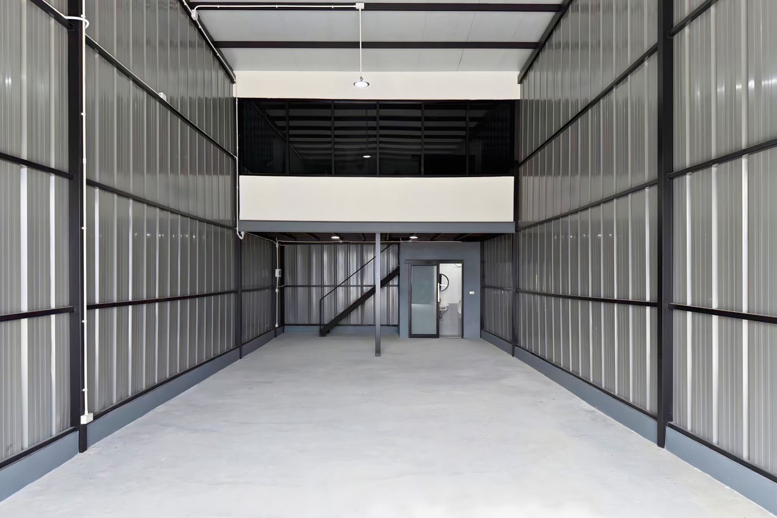 Warehouse for rent in Bang Phli, Samut Prakan - High-ceiling warehouse interior with steel frame, mezzanine level, staircase, concrete floor, and a private restroom door.