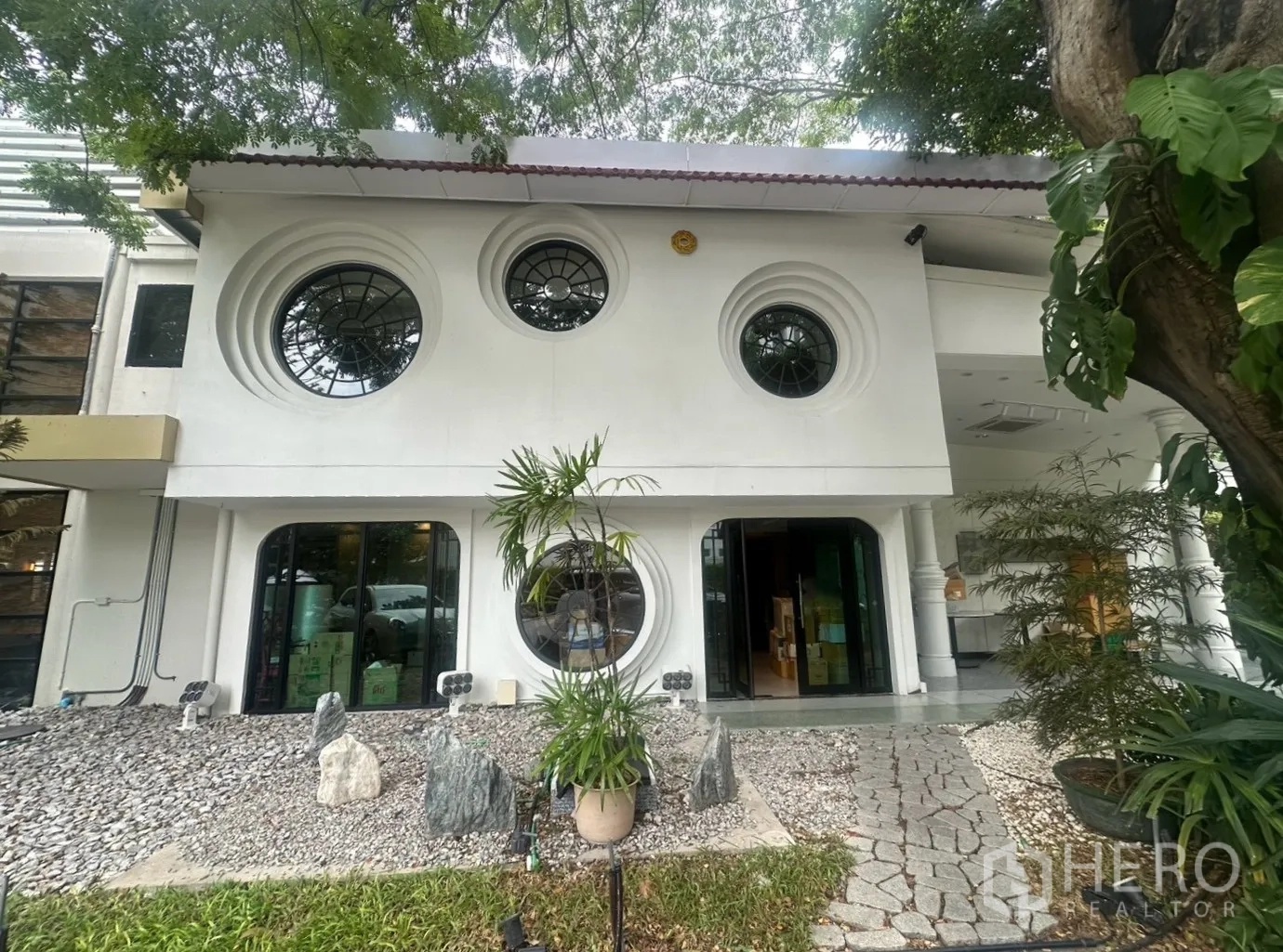 บ้านเดี่ยว for rent in Watthana, Bangkok - ด้านหน้าบ้านสองชั้นสีขาว หน้าต่างวงกลม และสวนกรวดจัดแต่ง.
