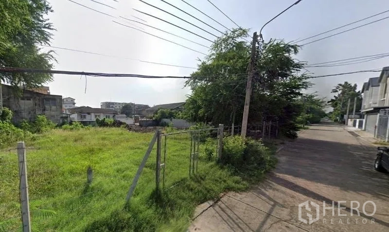 Land for rent in Khlong Toei, Bangkok - Corner view of the green plot facing a paved road with utility poles and cables in Khlong Toei.