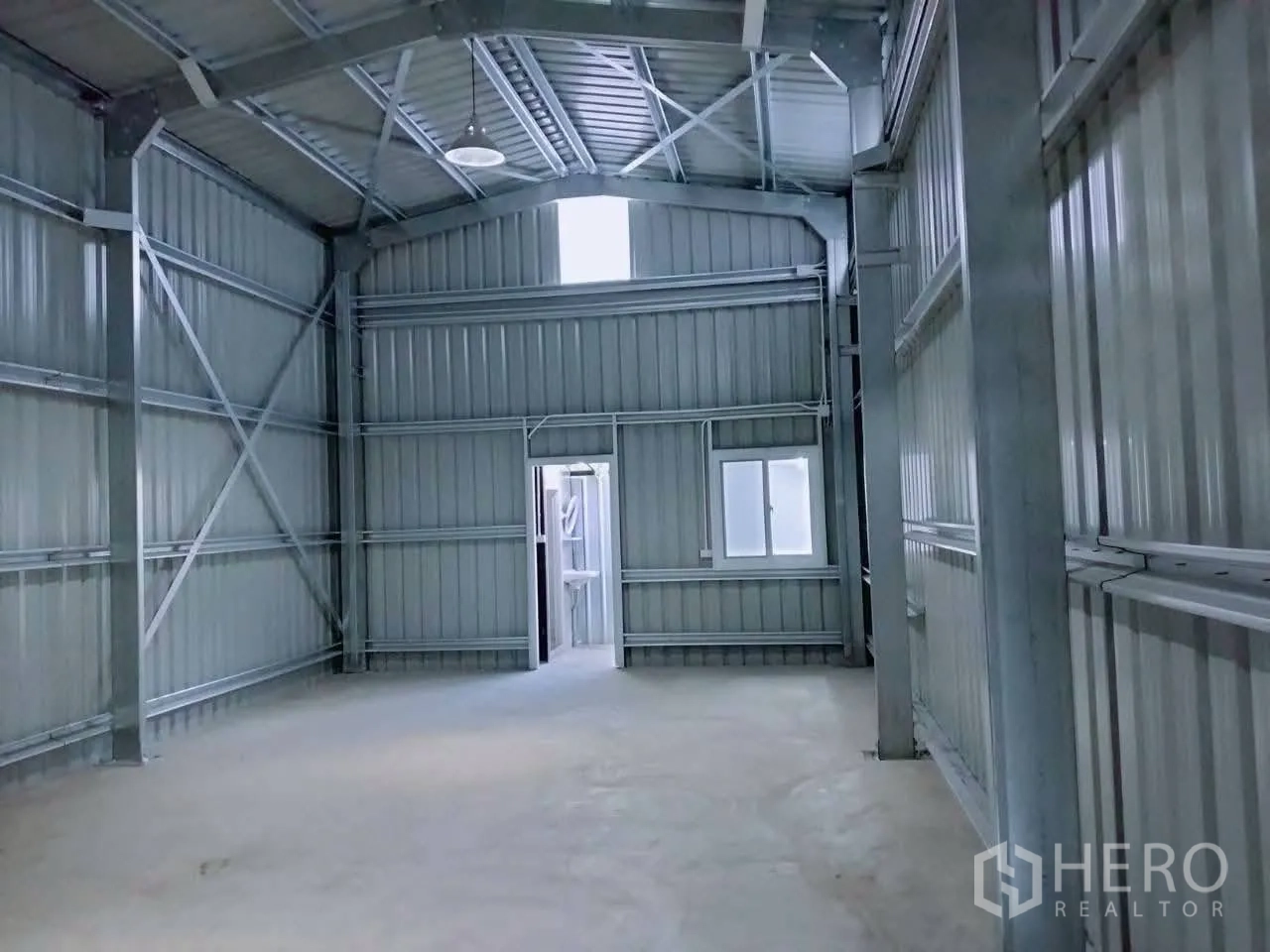 Warehouse for rent in Lat Phrao, Bangkok - High-ceiling steel-frame warehouse interior with concrete floor, door and window, and skylight.