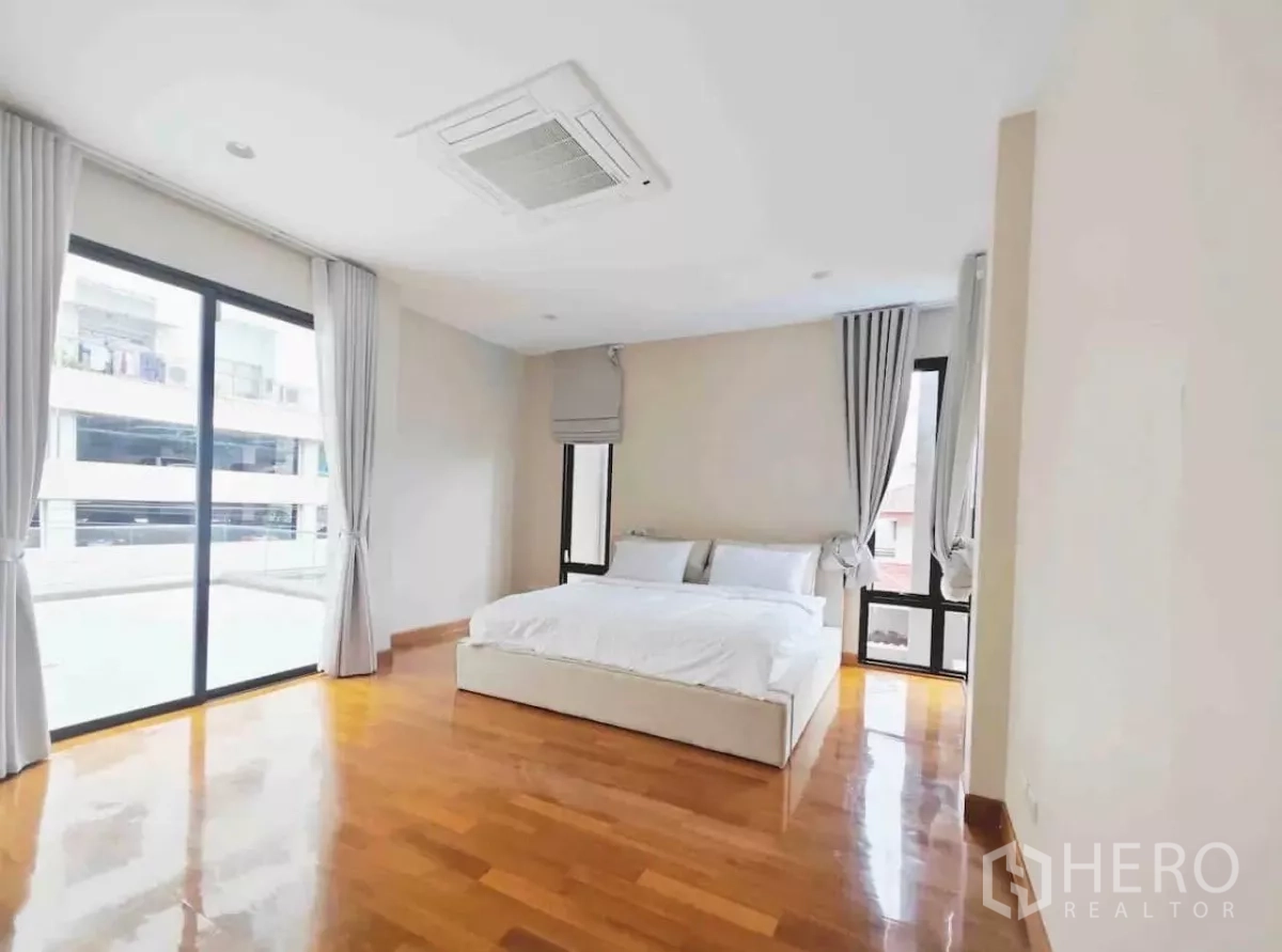 Detached House for rent in Phaya Thai, Bangkok - Corner bedroom with glossy timber floor, panoramic windows and grey curtains.