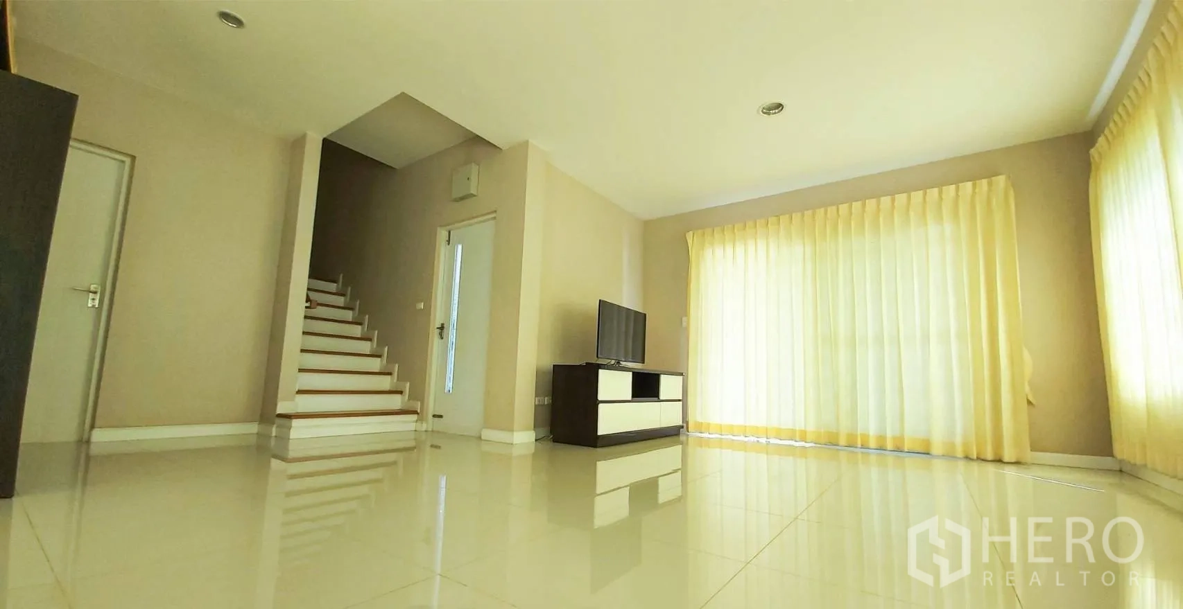 Detached House for sale in Bang Kapi, Bangkok - Living room view toward the staircase with TV unit and cream curtains.