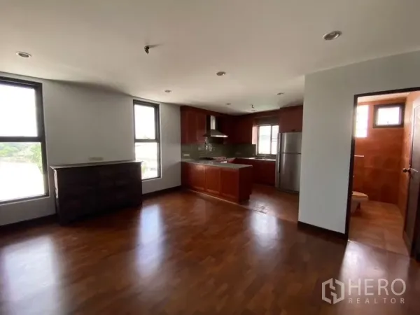 Home Office for rent in Phra Khanong, Bangkok - Open-plan living and kitchen area with wooden floors, built-in cabinetry, stainless refrigerator and an adjacent tiled bathroom.