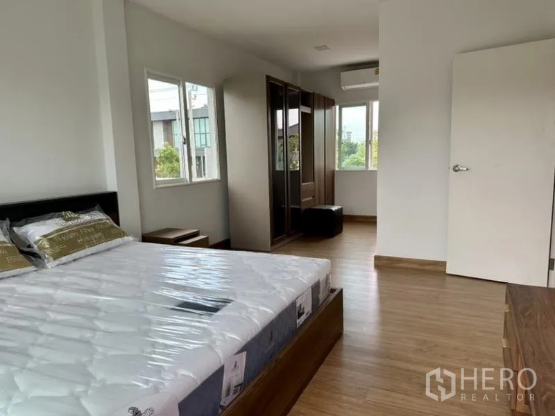 Townhouse for rent in Bang Phli, Samut Prakan - Spacious bedroom with bed, wardrobes, air conditioner and wood floors.