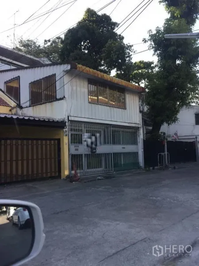 联排别墅 出售在Watthana, Bangkok - 两层联排住宅外观，金属推拉门与防盗窗，安静小巷与树木，临近BTS Ekkamai。