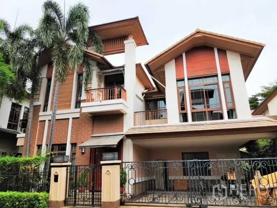 Detached House for rent in Watthana, Bangkok - Contemporary three-storey detached house in Watthana with gabled roof, balconies, gated entry and carport among palm trees.