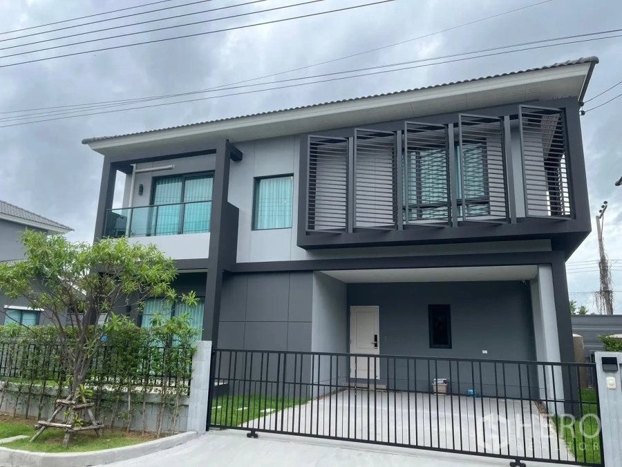Detached House for rent in Bang Phli, Samut Prakan - Modern two-storey detached house with balcony, sunshade screens and a gated carport.