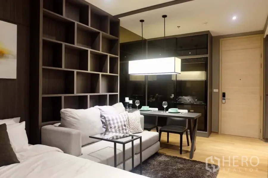 Condominium for rent in Khlong Toei, Bangkok - Living and dining area with pendant light, two-seat table, built-in shelving and entry door in a modern condo.
