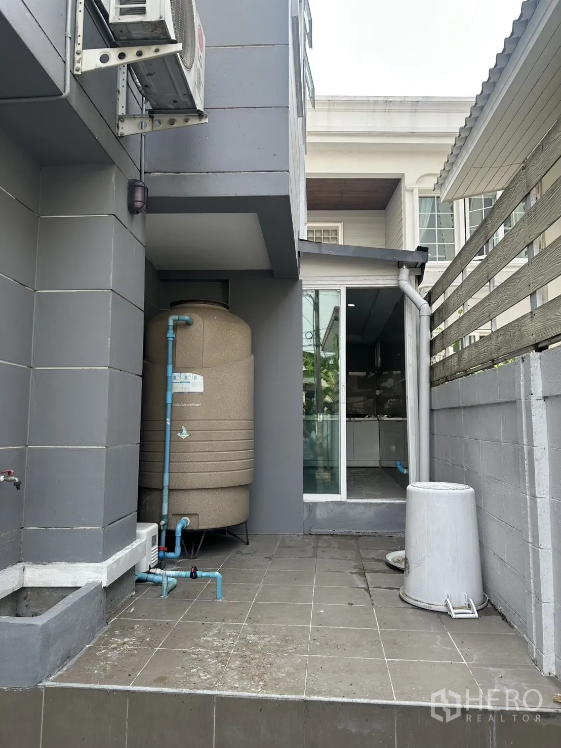 Home Office for rent in Watthana, Bangkok - Outdoor utility area with water tank, blue piping, tiled floor and sliding glass door to the interior.